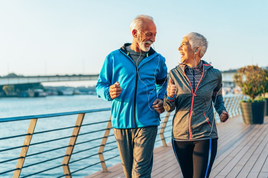 older man and women jogging on boardwalk near water