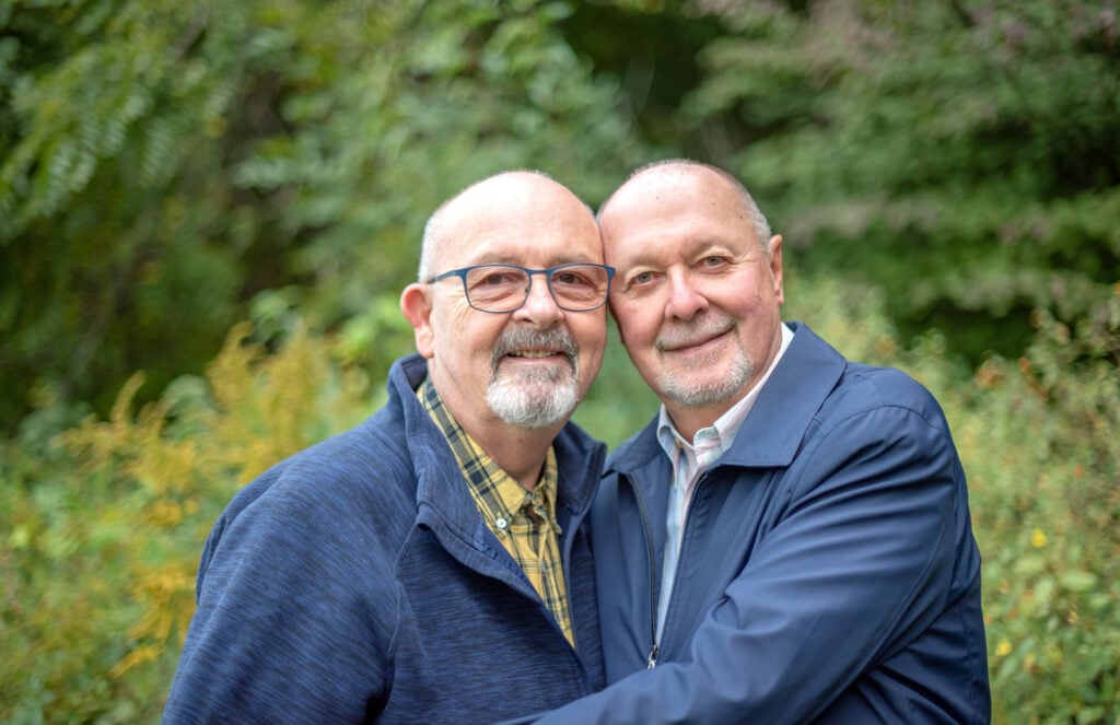 Senior male married couple smile in a nature-filled background