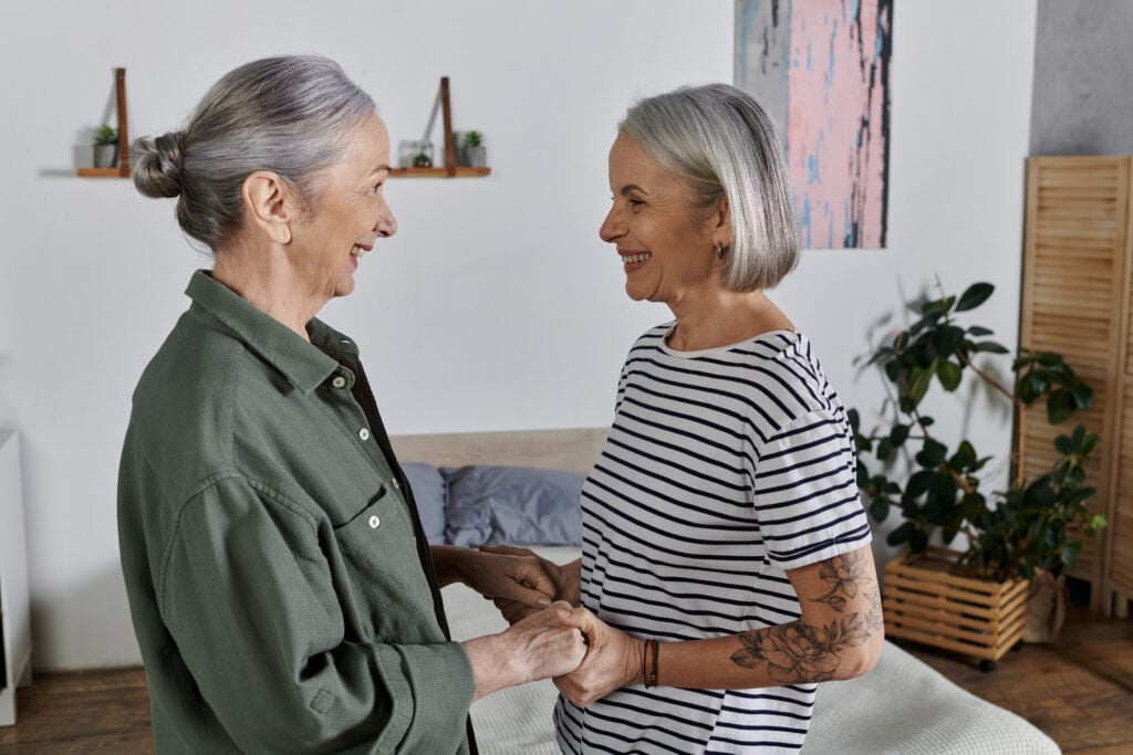 Senior women holding hands in a loving embrace, at home in their living room