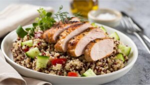 A delicious dish featuring grilled chicken slices atop a quinoa salad with fresh cucumbers and tomatoes, garnished with herbs.